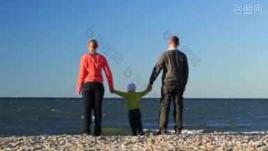 年轻的家庭在海边，一个可爱的小孩和他的父母站在沙滩上俯瞰